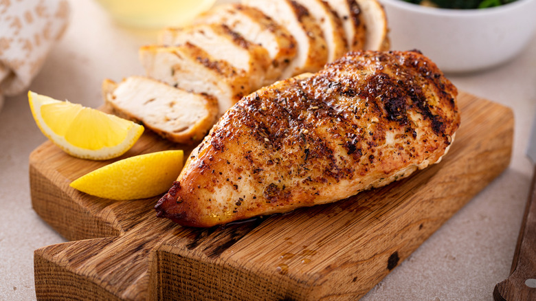 Grilled chicken breast on cutting board with lemon slices