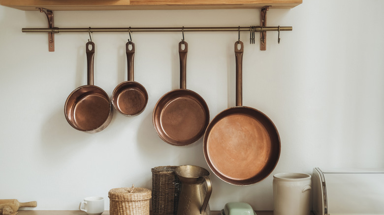 Copper kitchen pans hanging from a wall shelf