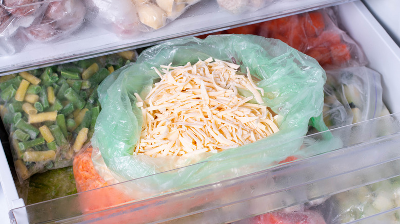 Various prepped and frozen food in bags, with an open bag of frozen shredded cheese in the middle