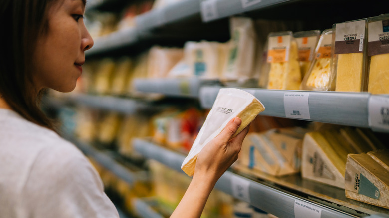 Woman standing in a grocery store holding a wedge of Brie in front of cheese shelves