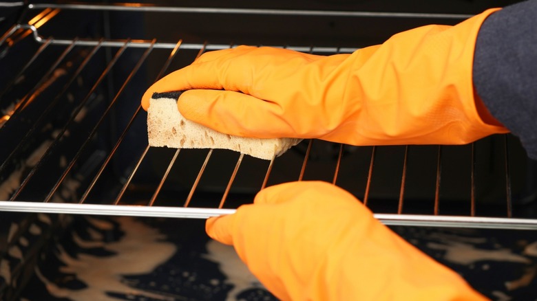 Gloved hands cleaning oven racks with a sponge