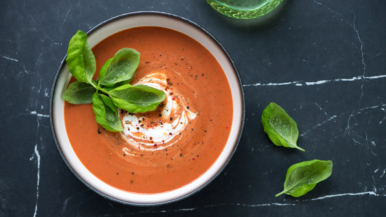 A bowl of tomato soup garnished with basil leaves.
