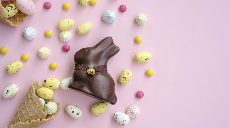 A chocolate bunny, candy eggs, and two ice cream cones on top of a pink background