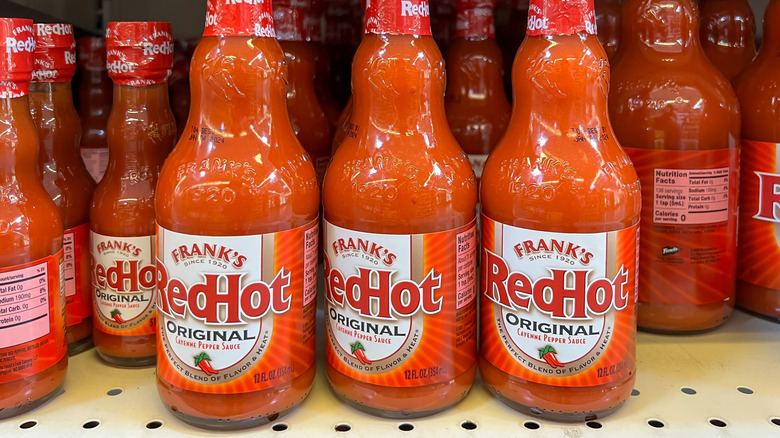 Three bottles of Frank's Red Hot on a supermarket shelf.