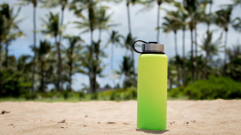 gradient green water bottle sitting on a beach