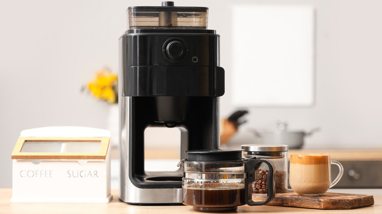 Drip coffee maker with pot and cup of coffee, plus coffee beans