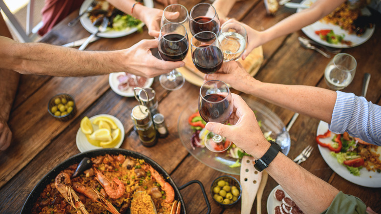 People toasting glasses of wine over paella