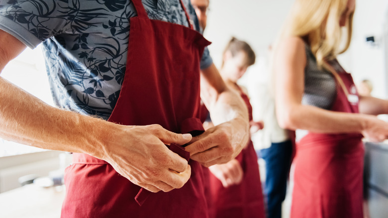 A man tying the strings of a red apron around his waist