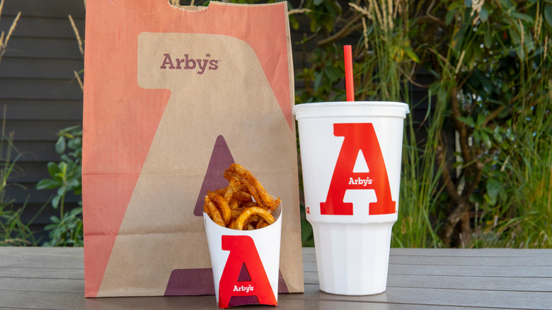 An Arby's order in a paper bag next to an Arby's drink carton and a portion of curly fries