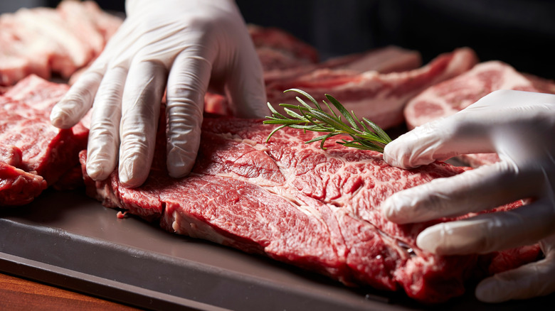 butcher handling raw beef brisket with gloved hands