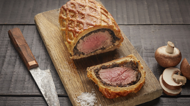 A sliced beef Wellington on a wooden cutting board.