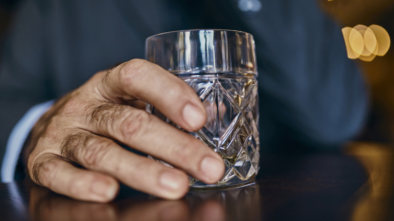 A person's hand holds a tumbler, also called a rocks glass.