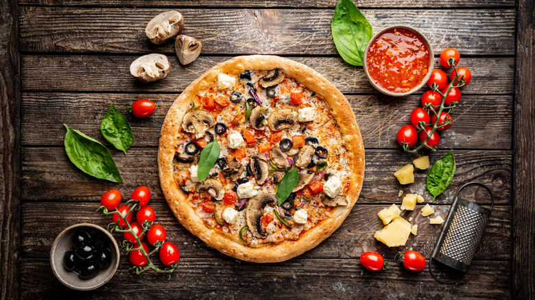 Veggie pizza surrounding by a variety of whole toppings