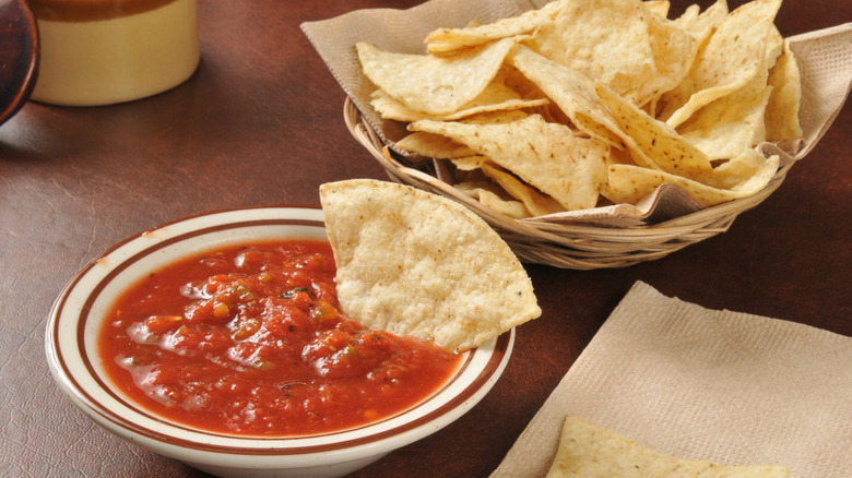 Bowl of salsa with tortilla chip next to basket of tortilla chips