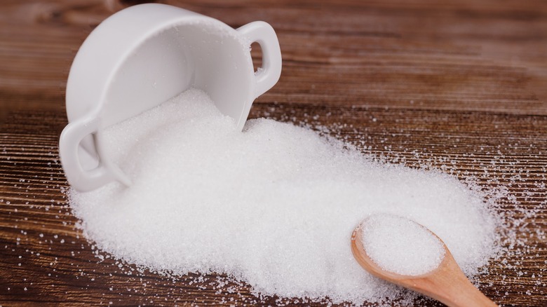 A tipped-over bowl of sugar has a wooden spoon next to it.