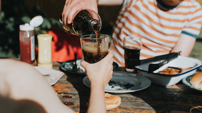 Person topping off a glass of cola for friend