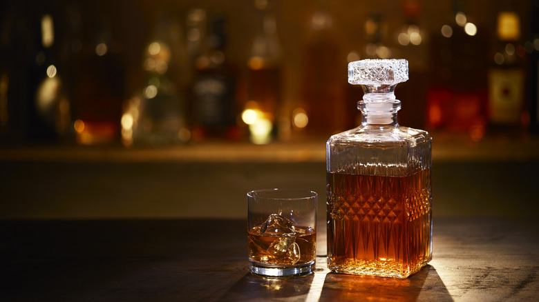 A bourbon bottle and a glass of bourbon on the rocks sit on a wooden bar