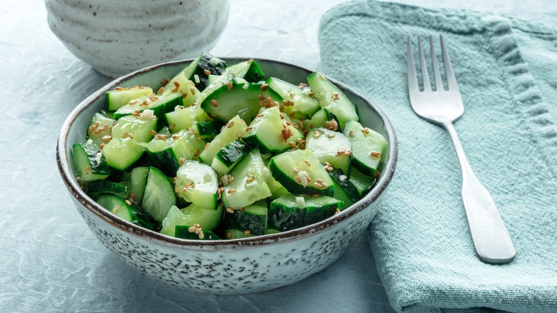 Homemade smashed cucumber salad topped with toasted sesame seeds sit in a bowl next to a fork