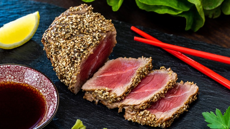 Sesame crusted tuna steak with chopsticks, side of soy sauce, greens, and lemon wedge