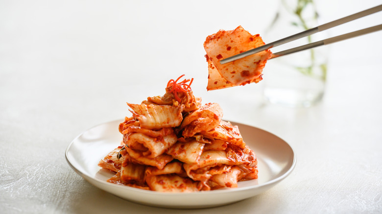 Someone using chopsticks to pick up kimchi from a plate