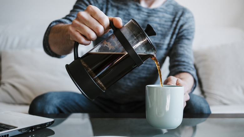 Hands pour French press coffee into cup