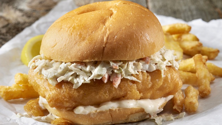 A piece of perfectly fried fish sits between buns with tartar sauce and creamy coleslaw.