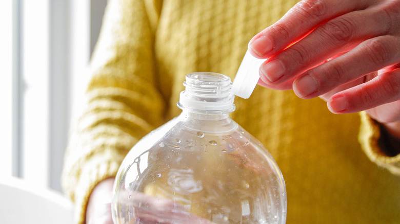 A person in a yellow shirt removes the cap from a plastic water bottle