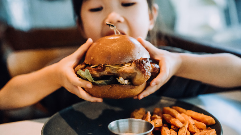A young girl preparing to take a bite out of a burger.