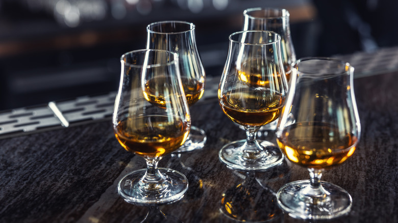 Five snifter glasses of whiskey sitting on a bar top