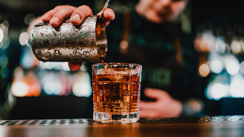 Bartender pouring a brown mixed cocktail into a highball glass