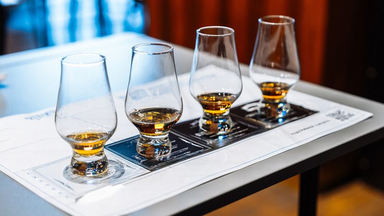 Four whiskey glasses are arranged in a row for a tasting.