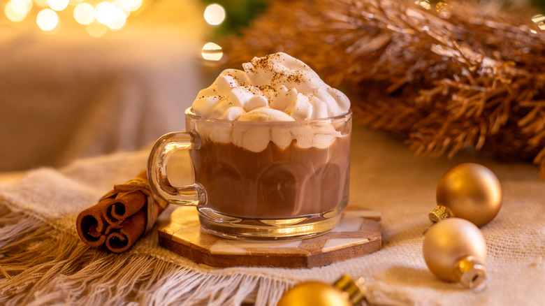 A cup of hot chocolate with whipped cream and Christmas-y decor
