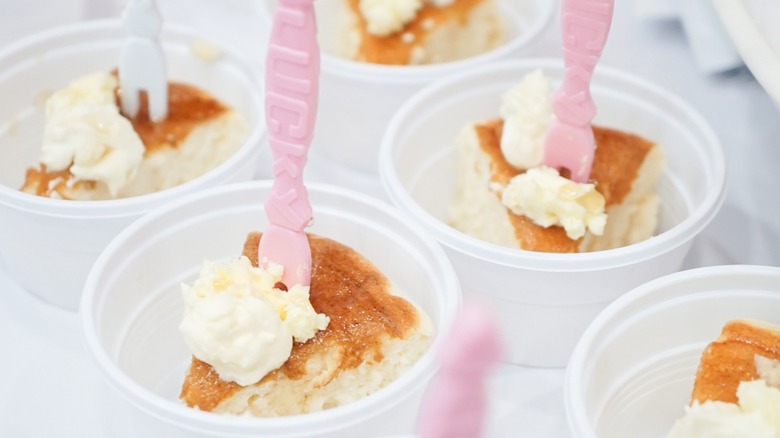Free samples of cheesecake with whipped cream are arranged in plastic ramekins.