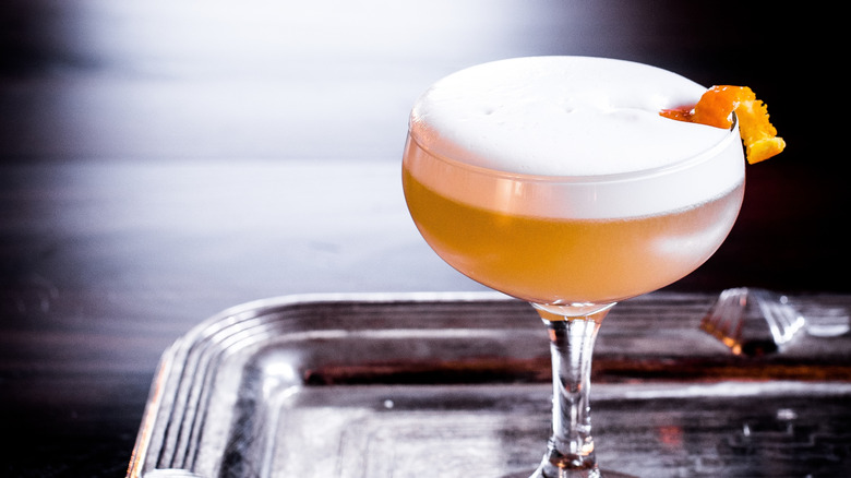 A frothy whiskey sour served in a coupe on a silver tray.