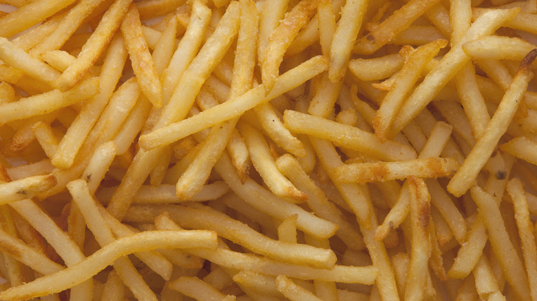 A close-up of fresh fried, golden brown, french fries piled up.
