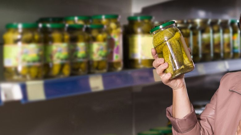 Person choosing a jar of pickles from the grocery store shelves