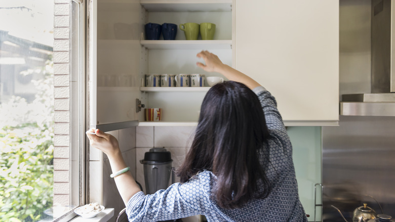 A person seen from the back reaching into a kitchen cupboard