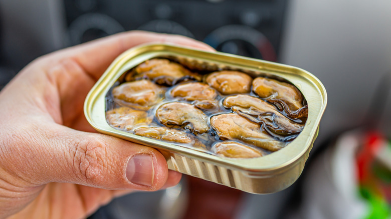 Hand holding canned oysters in oil