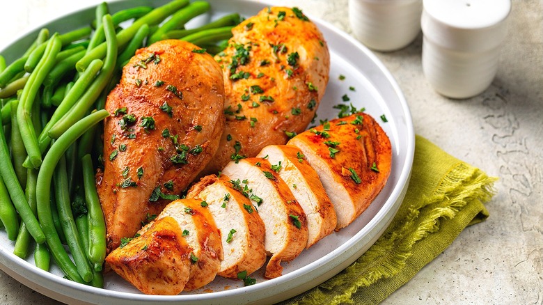 Seasoned and baked chicken breasts with green beans on white plate