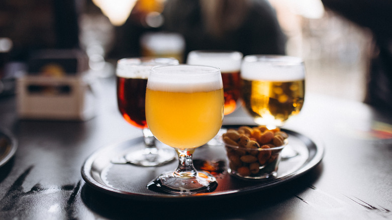 Full, fancy beer glasses are arranged on a tray with a small bowl of nuts.