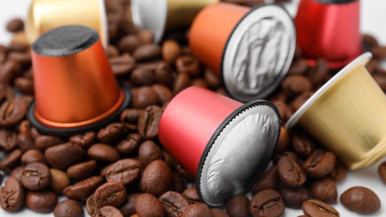 Assorted espresso pods lie among coffee beans.