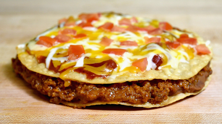 A Taco Bell Mexican pizza topped with melted cheese and tomatoes