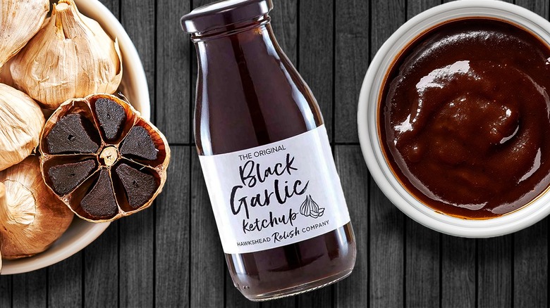 Bottle of black garlic ketchup beside black garlic cloves