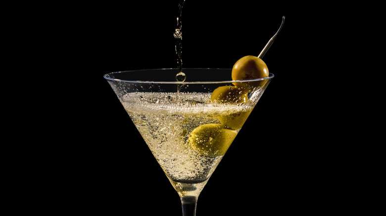 Liquid splashes into a martini with olives on a black background.