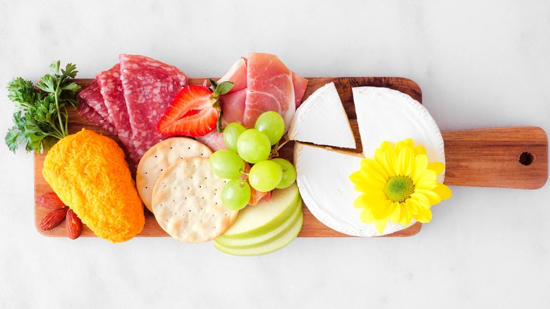 Carrot-shaped cheese ball on a wooden board with other cheeses, meat, and fruit