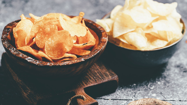Two bowls of different potato chip flavors on a wooden serving board