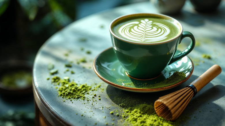 A cup of matcha latte with a frothing brush and powder on a small table