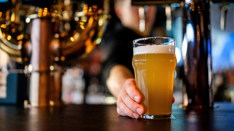 A bartender slides a glass of golden beer across a wooden bar top