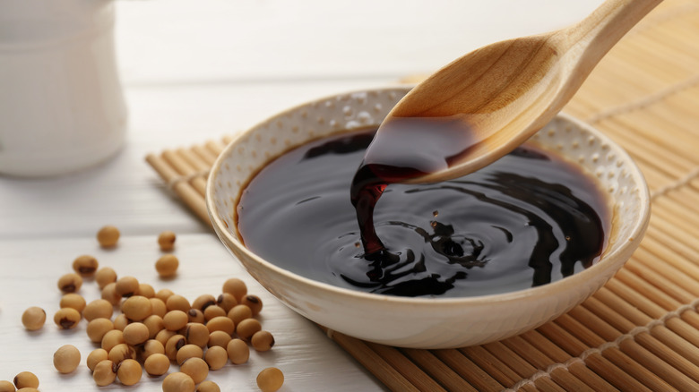 wooden spoon pouring soy sauce into small dish on bamboo mat