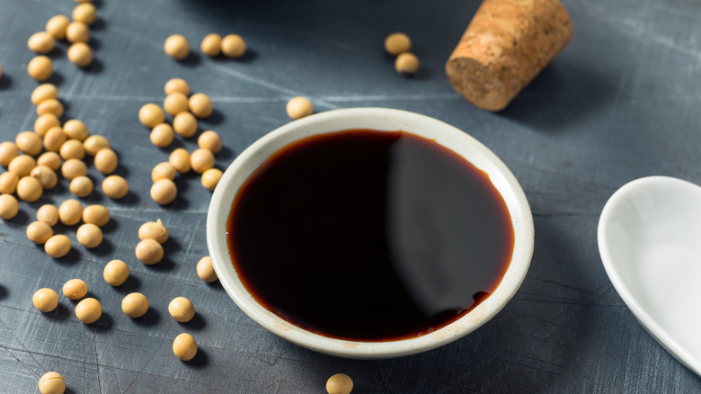 A bowl of dark liquid on a table surrounded by scattered soybeans